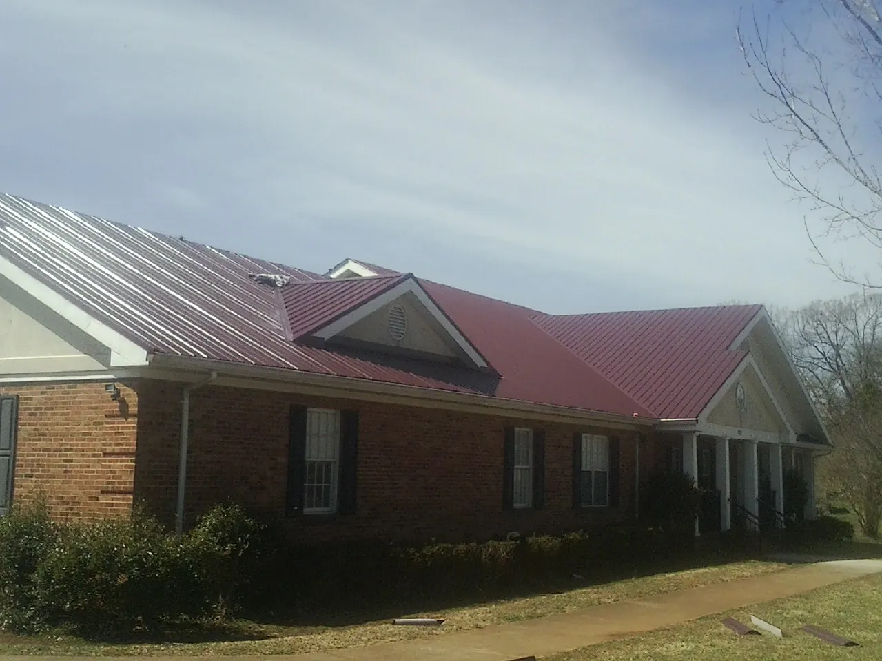 Red metal roof with gabled entries on a long brick building, from a Hail Damage Roof Repair job in Atchison