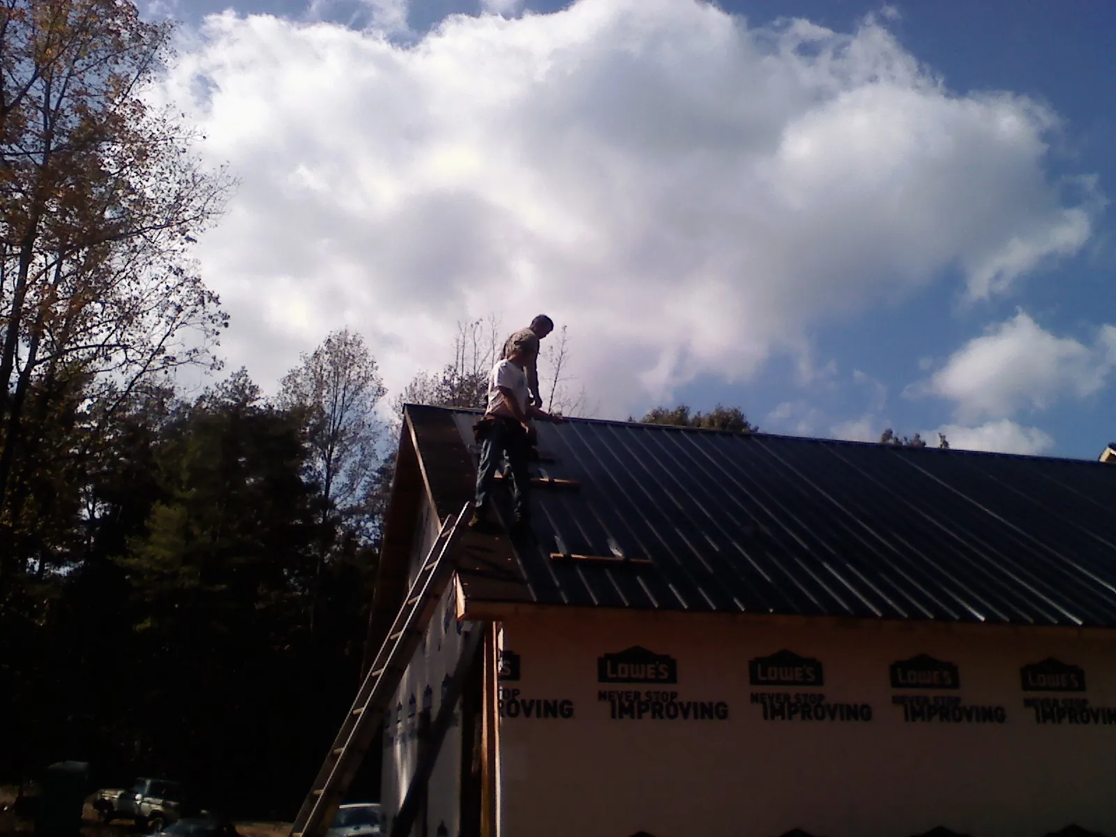Roofer fastening dark metal panels high against a cloudy sky, from a Roof Inspection job in Atchison